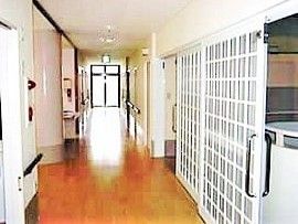 フローリング仕様の床と長く続く廊下が写っている。手すりが見えていて施設内の設備もある様子