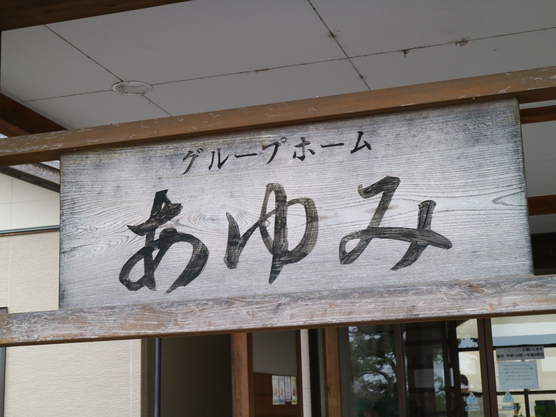 施設の玄関脇の壁に、木製の看板が掲げられている。大きな一枚板に黒い大きな文字で施設名が記載されている。