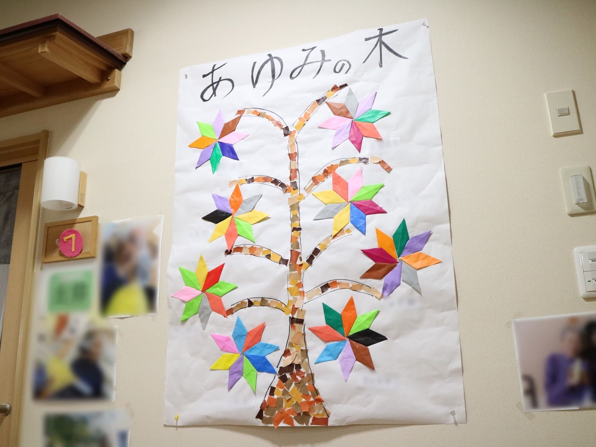 白い壁に飾られた大きな作品。白い紙に茶色の髪をちぎって貼った木の幹があり、その周囲に花が作られている。