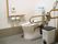 広めの個室タイプのトイレである。右奥に温水洗浄便座が設置された便座があり、その手前に折り畳み式の手すりがある。