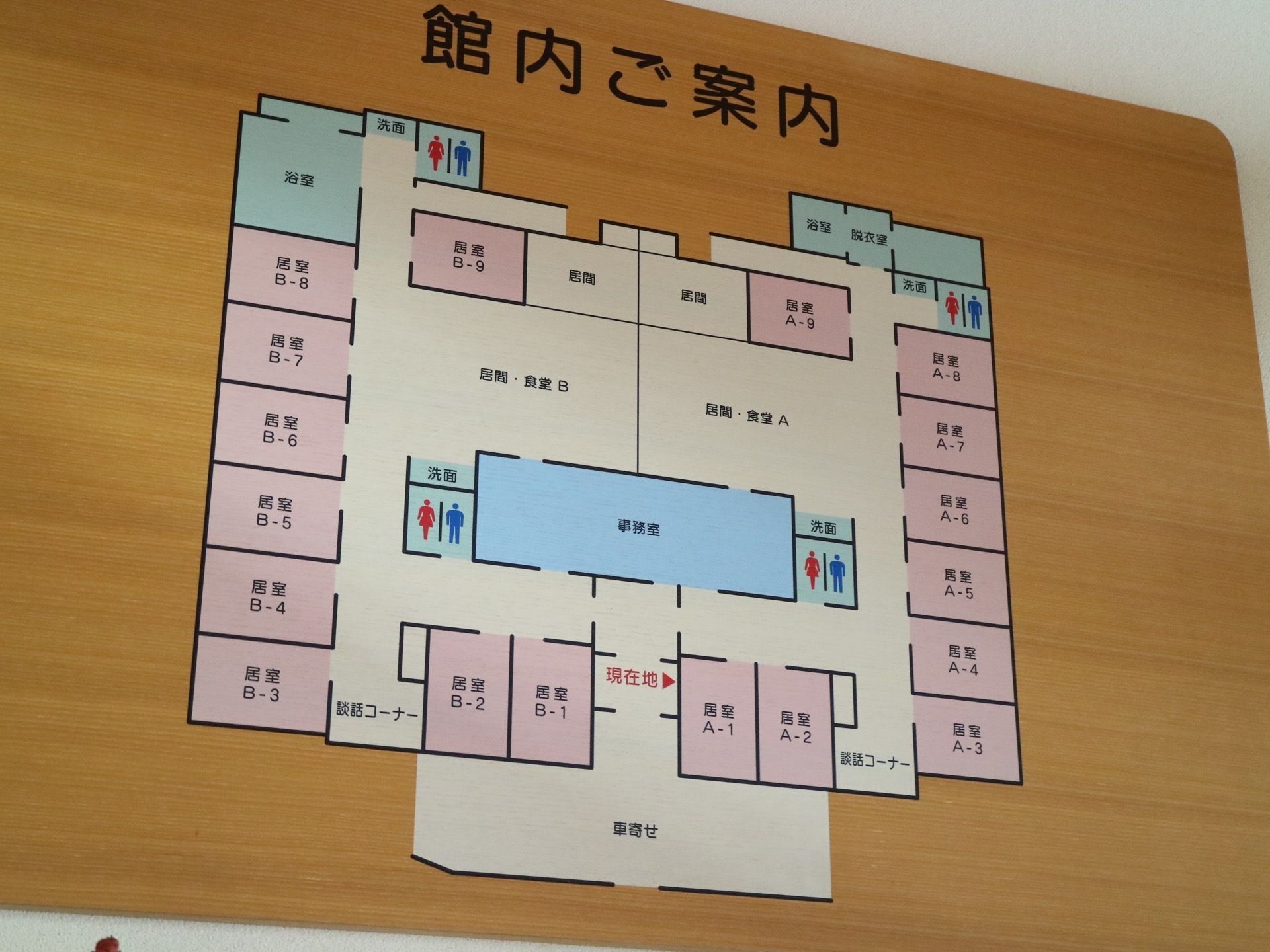 木材を使用して作られた館内案内図が壁に掛けられている。各居室はピンク、トイレなどの共用部は水色で塗られている。