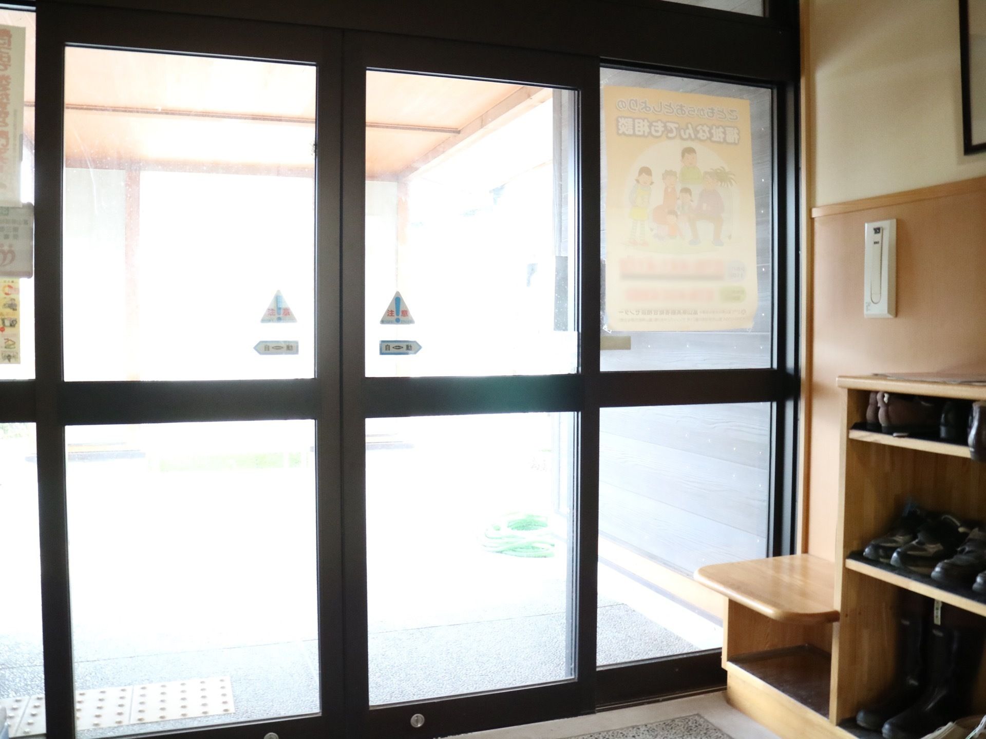 黒い枠にガラス窓のある入口で、自動扉になっている。右手の壁際に胸ほどの高さ前の下駄箱が作りつけられている。