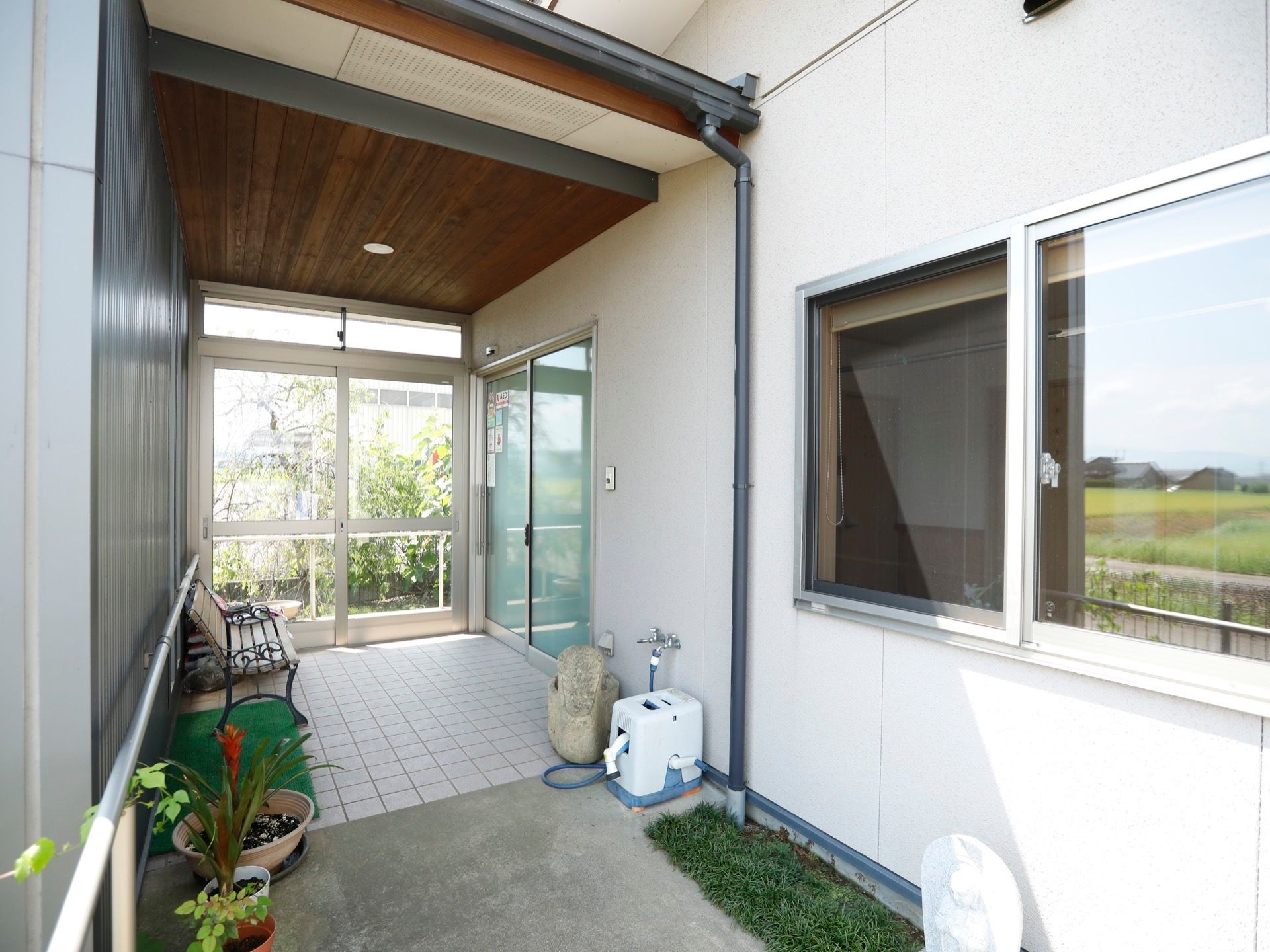 屋根が備え付けられた、エントランスである。天井に丸型の照明がある。壁側には手すりが設けられている。