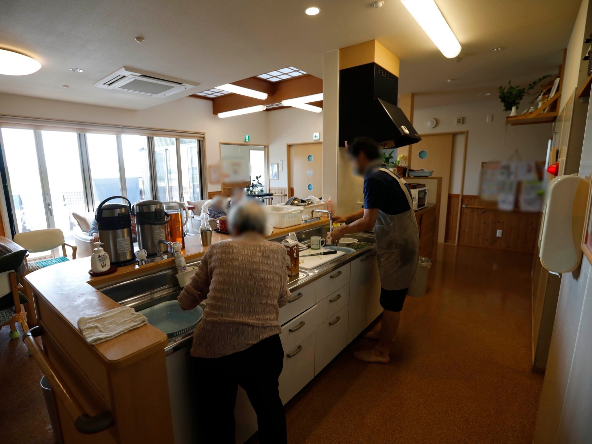 広く開放的な共有スペースに、おしゃれなシステムキッチンがある。スタッフと入居者様が作業を行っている。