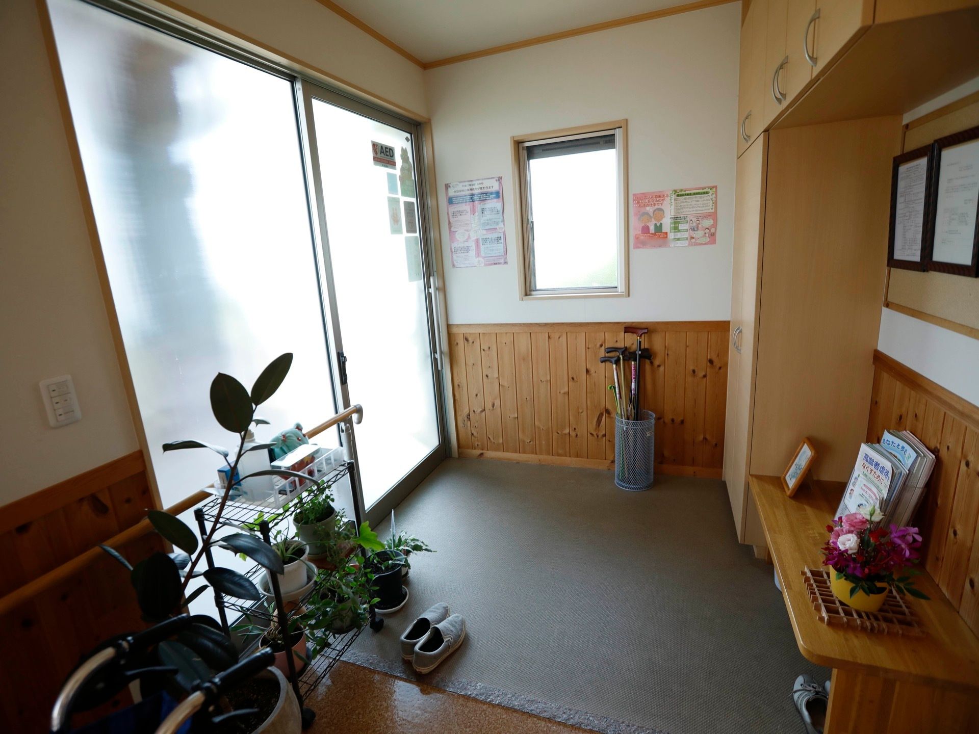 すりガラス式の、広々とした扉が設置された玄関である。壁に腰板が貼られているほか、手すりも備えられている。