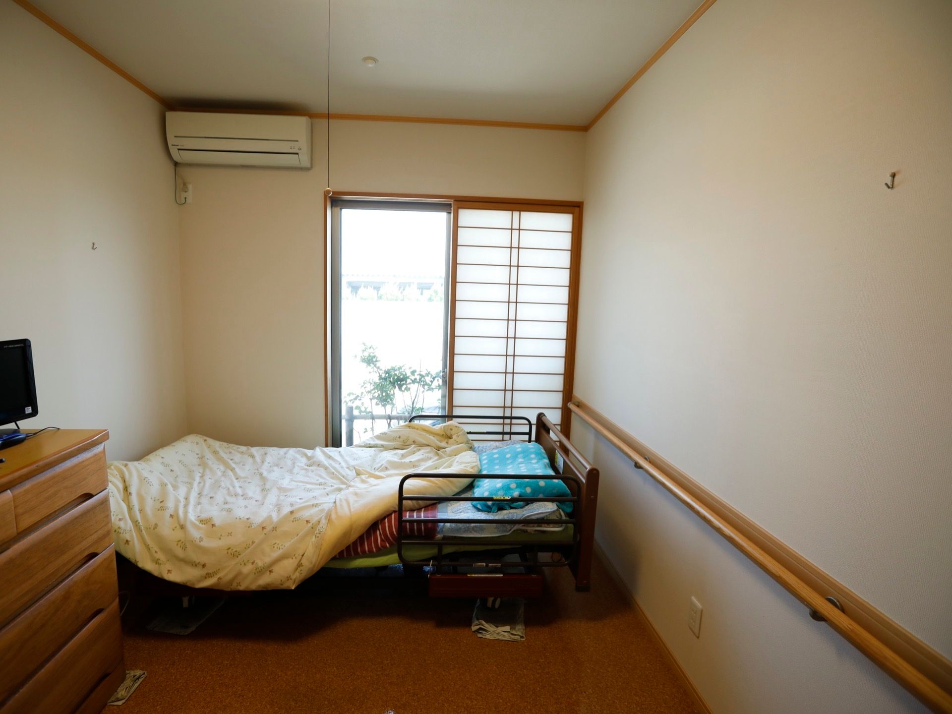 掃き出し窓に、格子扉が設置された居室である。サイドガードが設置された、介護ベッドを完備。エアコンも備えられている。
