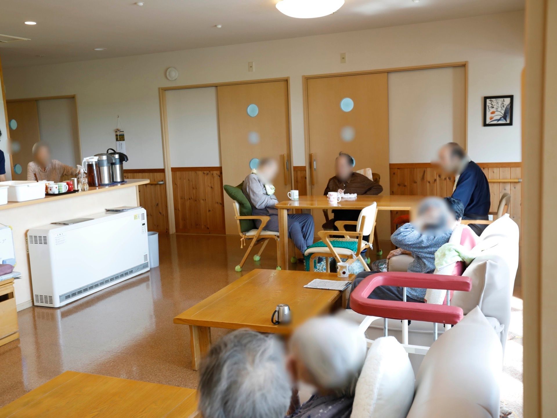 広々とした、ゆとりのある共有空間である。テーブル席やソファがある。入居者様がそれぞれ、自由にくつろいでいる。
