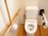 白色の洋式便座が備え付けられたトイレである。立ち座りをサポートする手すりが完備されている。可動タイプもある。
