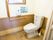 木製の腰板が貼られた、洋式のトイレである。Ｌ型の手すりやリモコンが備え付けられている。小窓も設置されている。