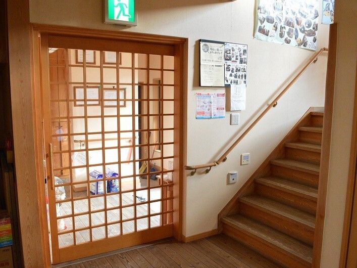 手すりが付いた木製の階段の壁にはたくさんの写真が飾られている。階段を降りたところには引き戸があり、玄関へと続いている。