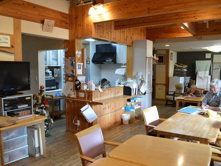 対面式キッチンからリビングダイニング全体を見渡すことができる。木製のテーブルに一名の入居者がついている。