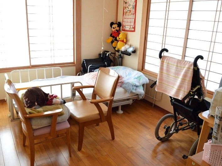 ぬいぐるみが飾られたフローリングの部屋には寝具付きのベッドがあり、シルバーカーやいすも置かれている。