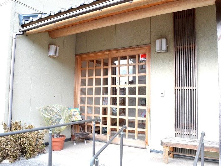 木製のベンチが置かれた玄関には手すりが付き、警備会社のステッカーが玄関のドアに貼られている。