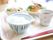 ある日の食事メニューである。明るい色調のプレートには、ご飯や主食が陶器の器に盛り付けられ、並べられている。