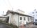 施設建物は１階建てである。同敷地内の母体病院の建物に明記された名称や居室のエアコンの室外機、駐車場に停車している車が見える。