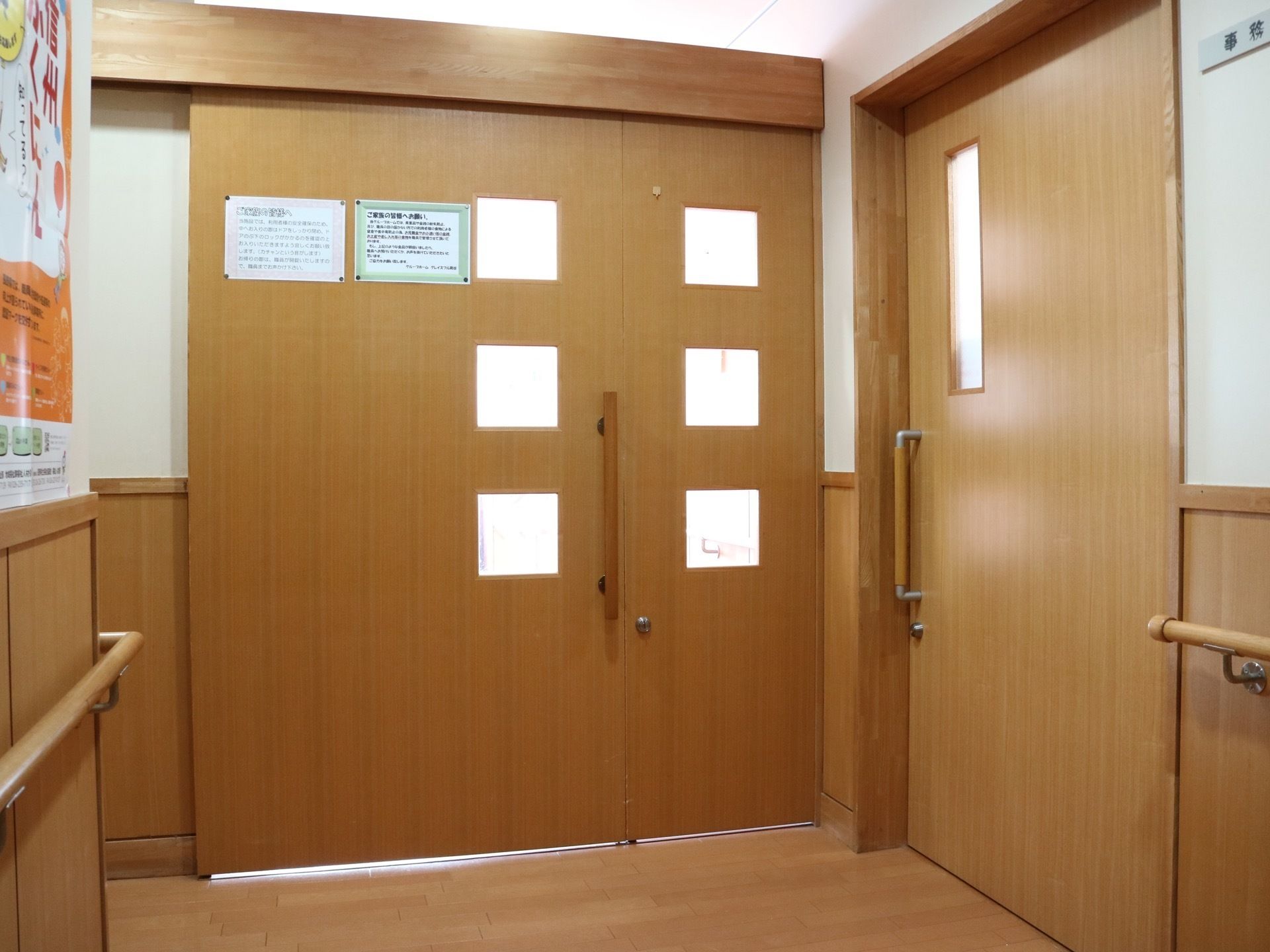 右手に事務室へ続く引き戸がある。正面にも扉があり、貼り紙がされている。四角い窓が６か所に開いており、光が漏れている。