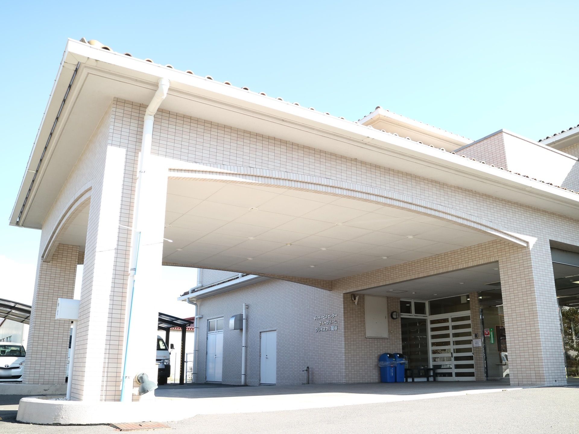 白いレンガ張りの外壁の大きな玄関ポーチの図である。太い柱で支えられ、緩やかなアーチを描いた屋根がある。