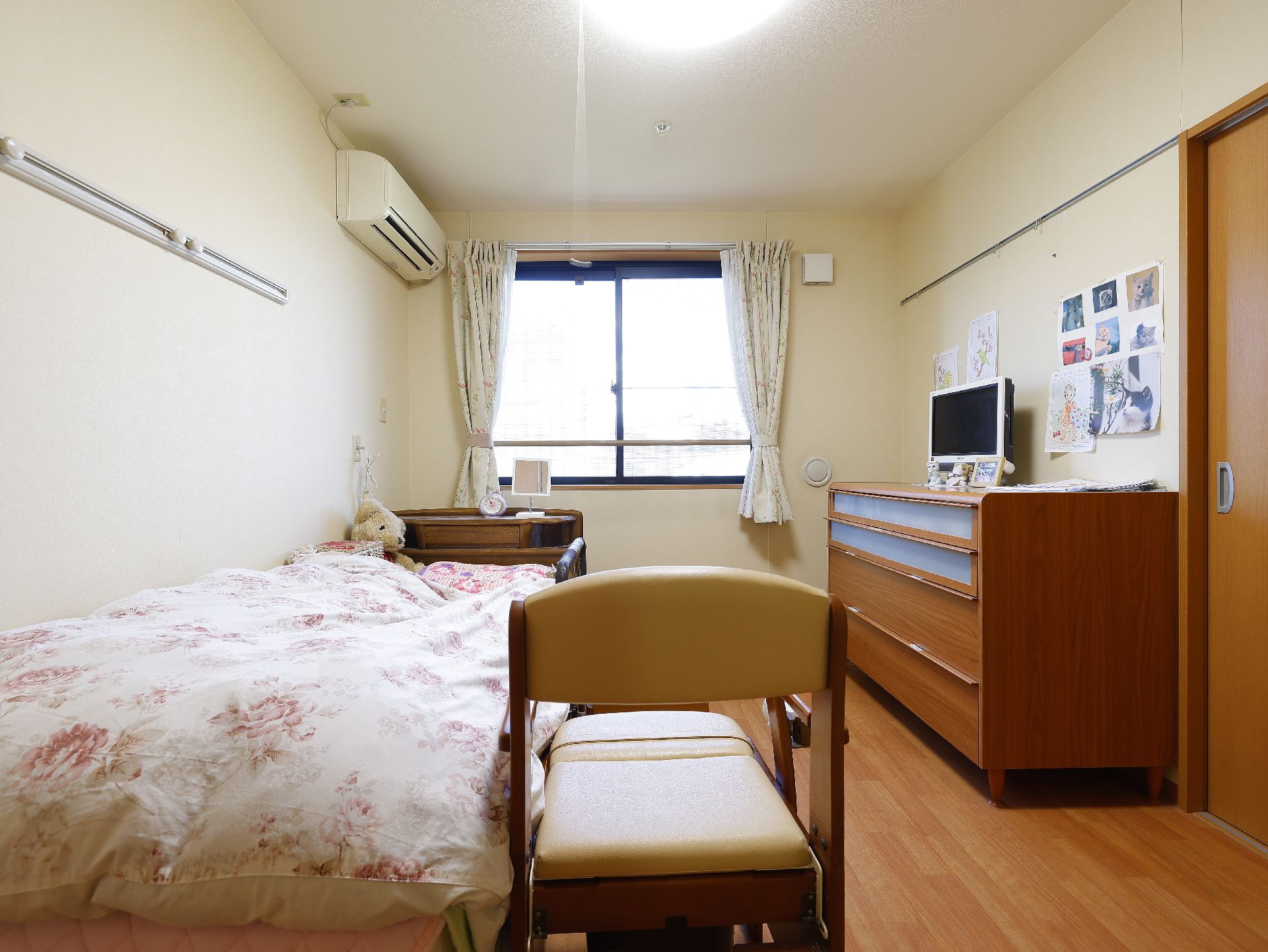 窓から光が入り、エアコン、介護ベッド、家具類が置かれている居室