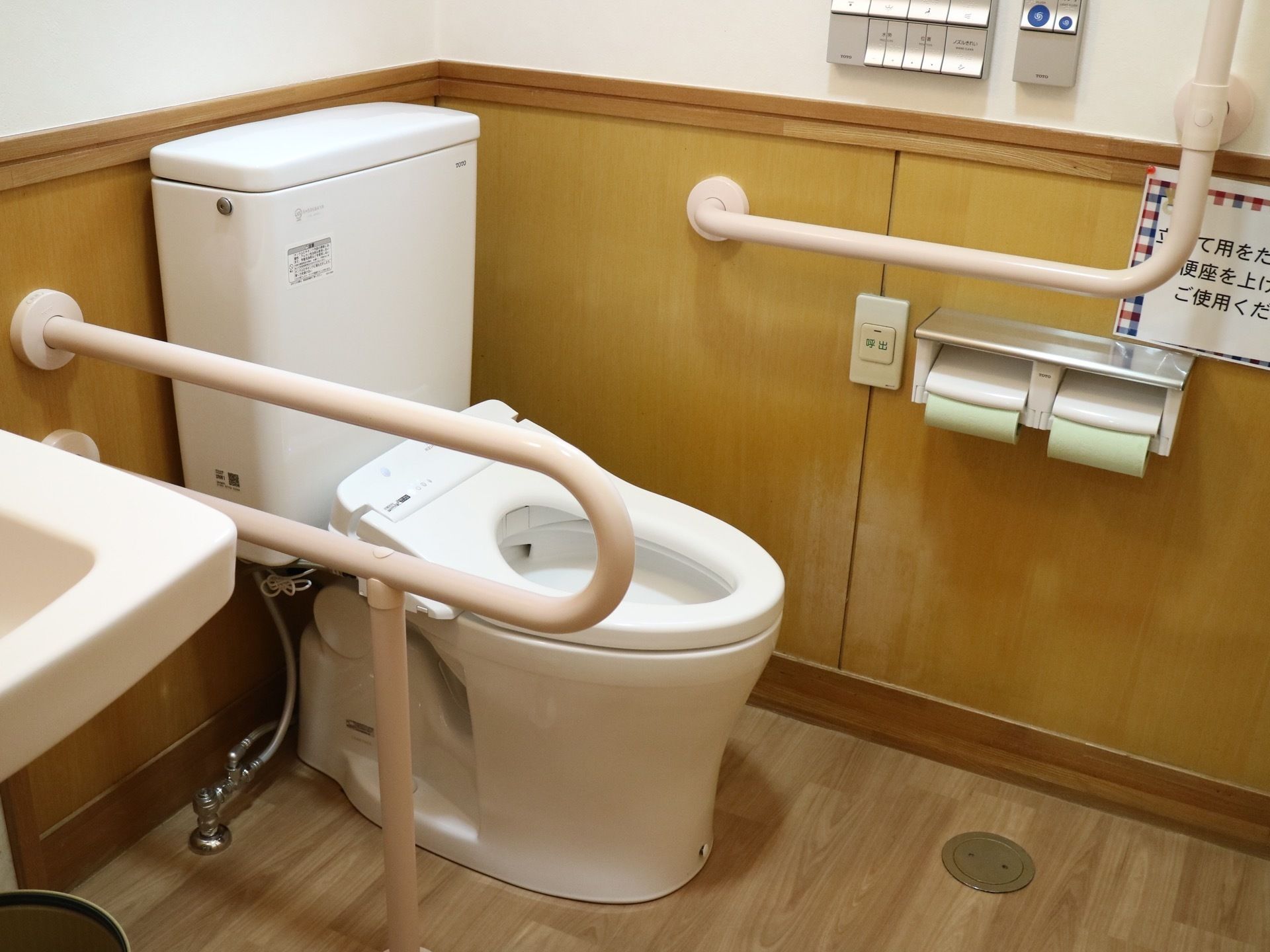 個室トイレである。中央にトイレがあり、温水洗浄便座が設置されている。奥の壁に操作パネルがある。