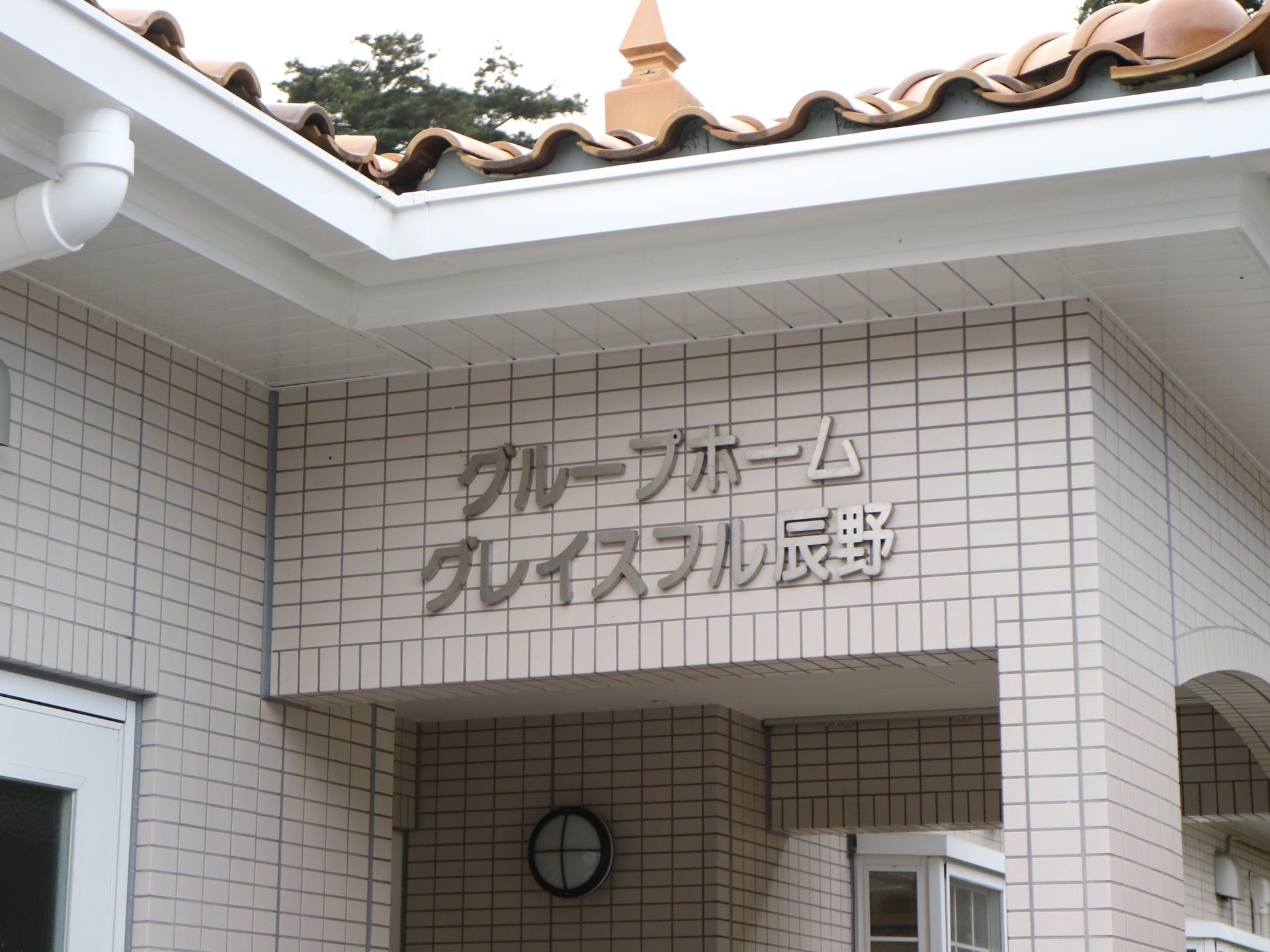 施設の外壁は白いレンガ材でおおわれており、玄関の屋根部分にはステンレス製の文字で施設名が表示されている。