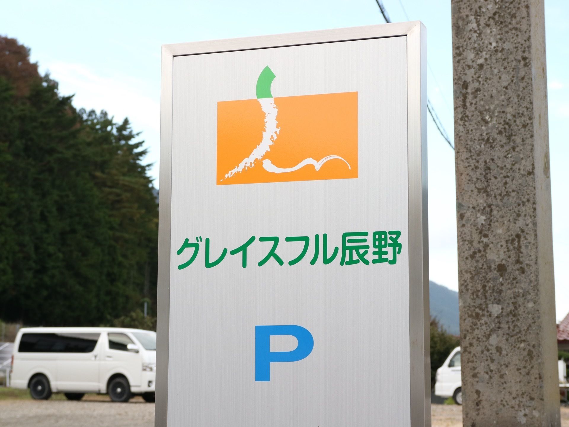 施設の敷地入口に大きな看板を設置している。白い板にオレンジと黄緑のロゴが描かれ、その下に緑の字で施設名が書かれている。