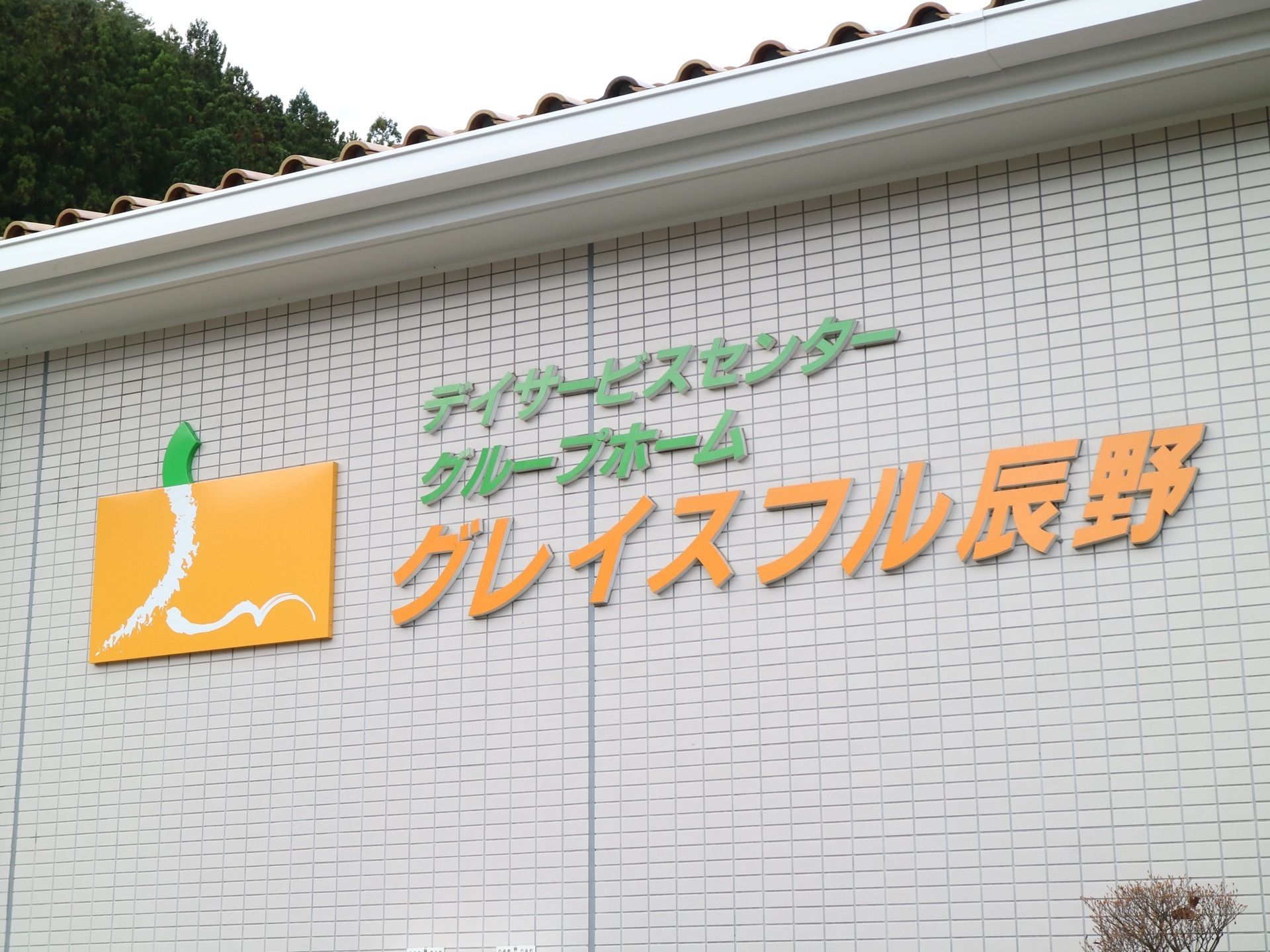 波を打った屋根が乗った施設で、１階部分の外壁にオレンジや緑色の文字で施設名やロゴが取り付けられている。