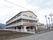 鉄骨造３階建ての建物の外観。周りはのどかな田園風景に囲まれている様子