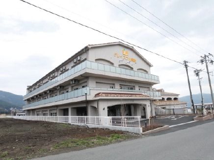 鉄骨造３階建ての建物の外観。周りはのどかな田園風景に囲まれている様子