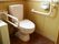 全面木目調の落ち着いた空間のトイレである。便器は全面ピンク色で、両脇に手すりがしっかりと固定されて設置されている。