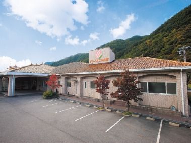 横に長い学校のような雰囲気の建物とその奥にある山々が写った写真。グループホームグレイスフル日義の外観