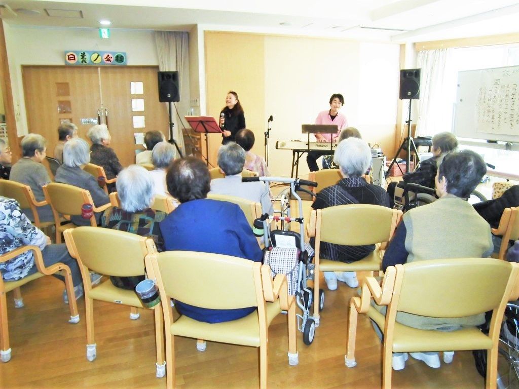 演奏会に集まっている高齢者の様子。前に出て演奏している人とそれを眺める高齢者