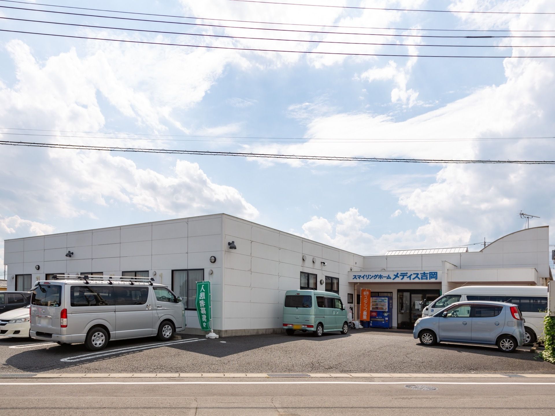 施設前には駐車スペースが完備されている。施設は1階建てになっており、道路に面している。玄関横に自動販売機が置かれている。