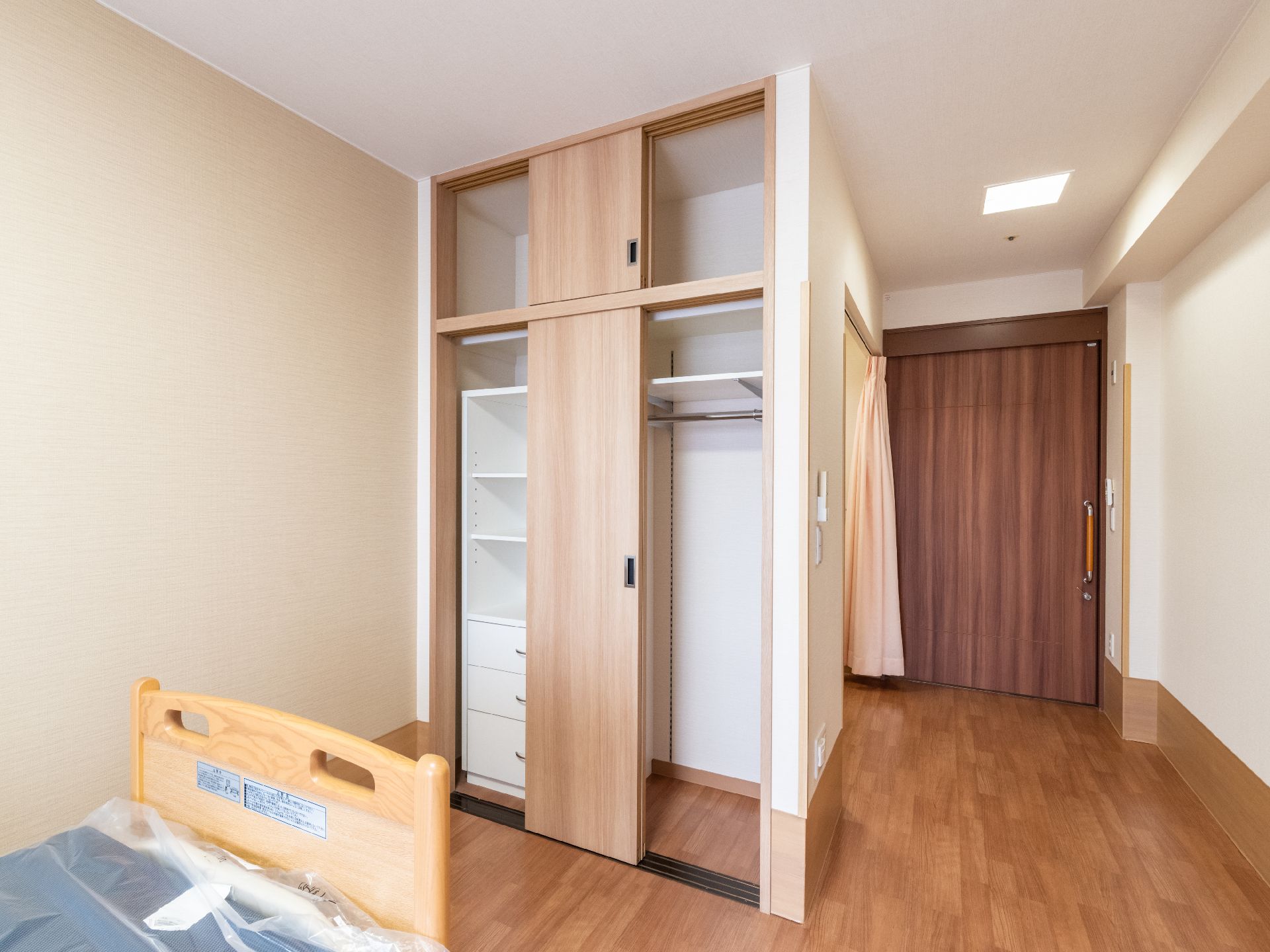 ベッドの置かれた部屋の白い壁に備え付けられた木製の扉のクローゼット
