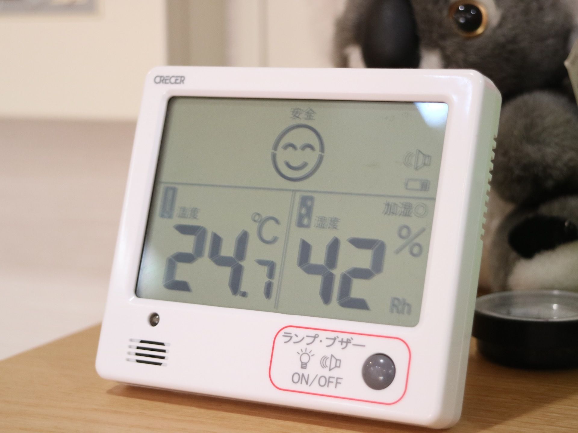 木製の棚の上に白いデジタル温度計が置かれている。温度と一緒に湿度も計ることができる。ランプが点くスイッチがある。