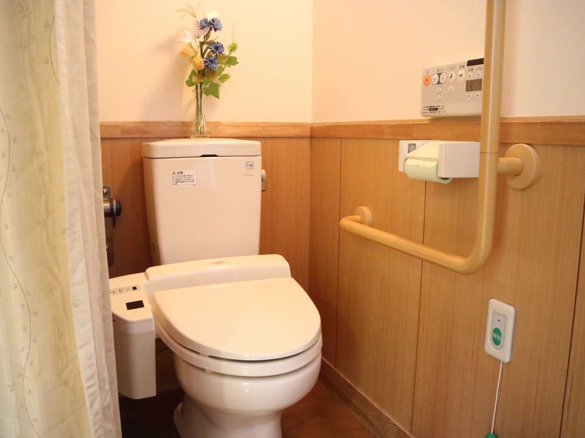 レールカーテンで開け閉めをする仕様で、中央に温水洗浄便座が設置されたトイレがある。右手の壁に手すりがある。