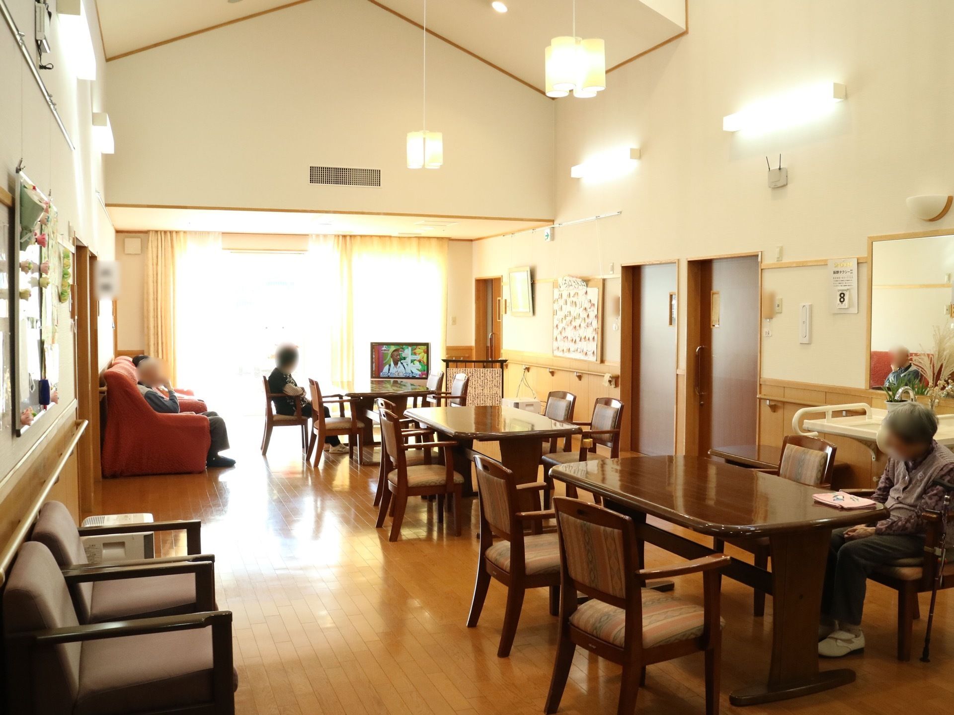 天井が屋根の形に吹き抜けになった共有スペースである。正面奥に大きな窓があり、その前に液晶テレビが置かれている。