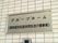 白いレンガ造りの外壁に、ステンレス製の板が埋め込まれている。黒い字で施設名が書かれている。看板の下にインターホンがある。