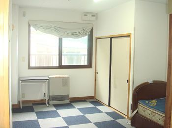 居室のフロアはチェック柄で押し入れが付いている。窓にはカーテンが付けられていて、ヒーターも置かれている。