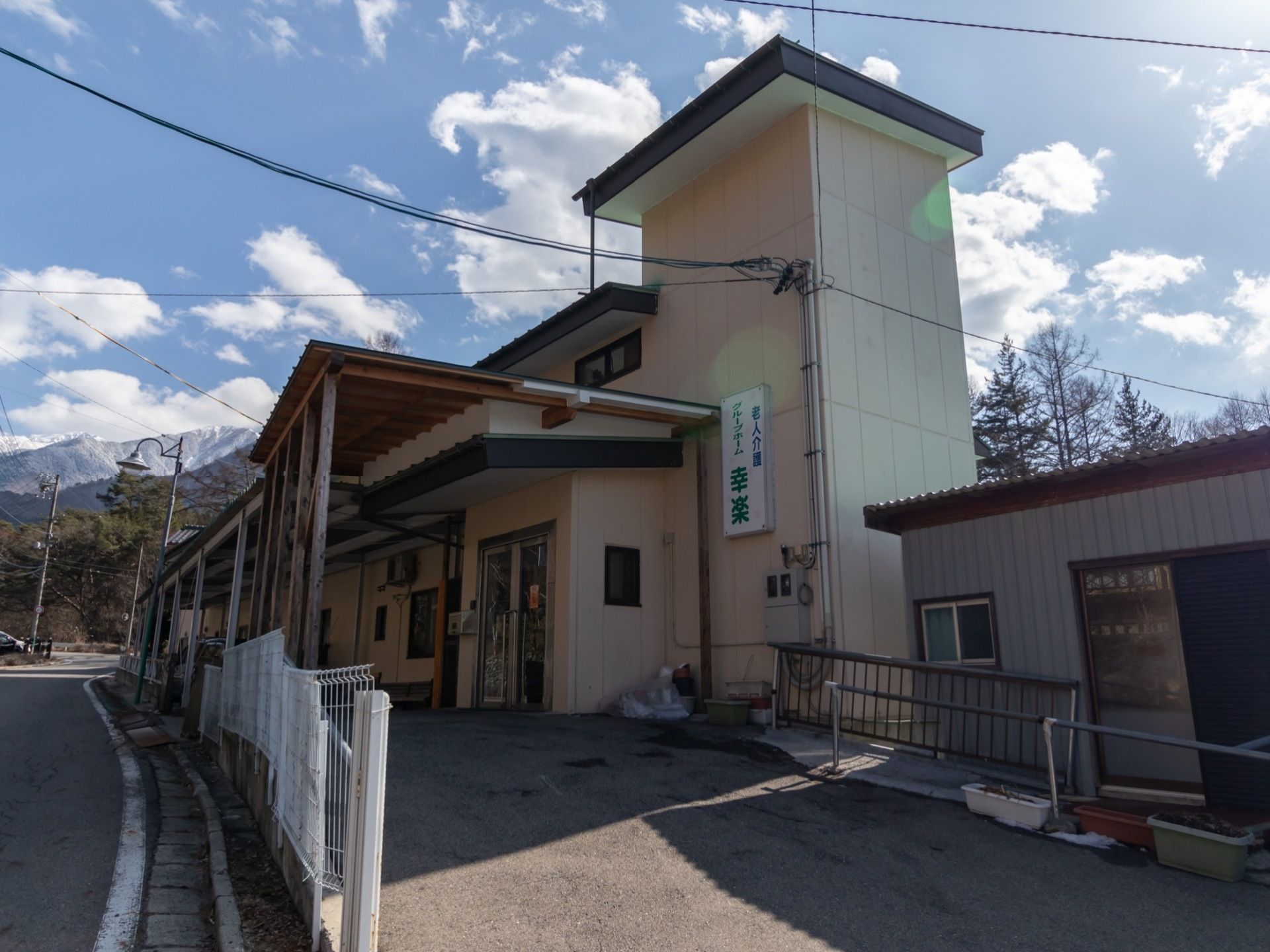 一軒家風の施設外観になっている。外壁には施設名が記された看板が設置されている。雨除けのひさしが施されている。