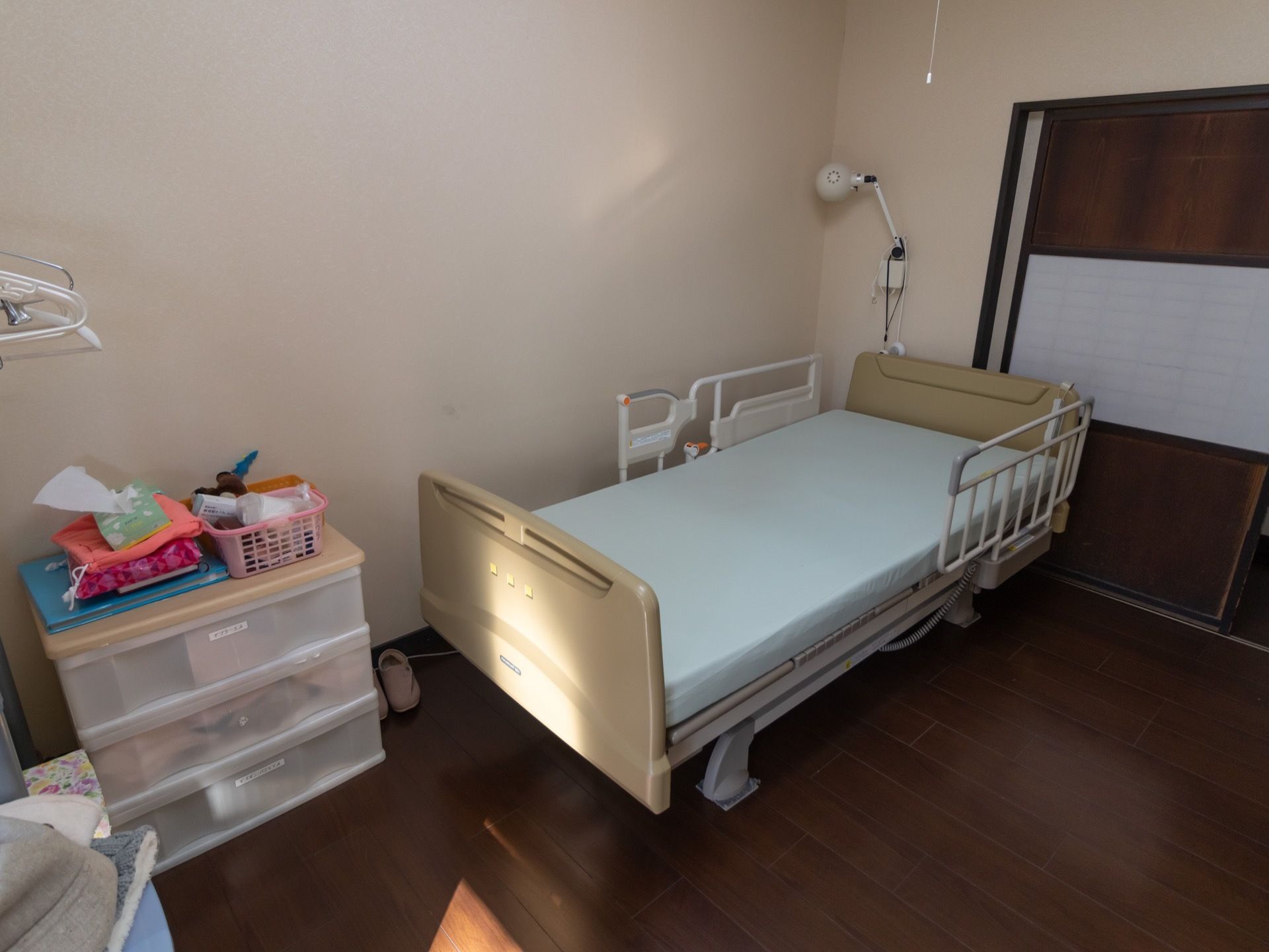 居室入口の引き戸には、中央部に障子の部分がある。室内には転落防止柵がついたベッドが置かれ、その隣には収納ボックスがある。