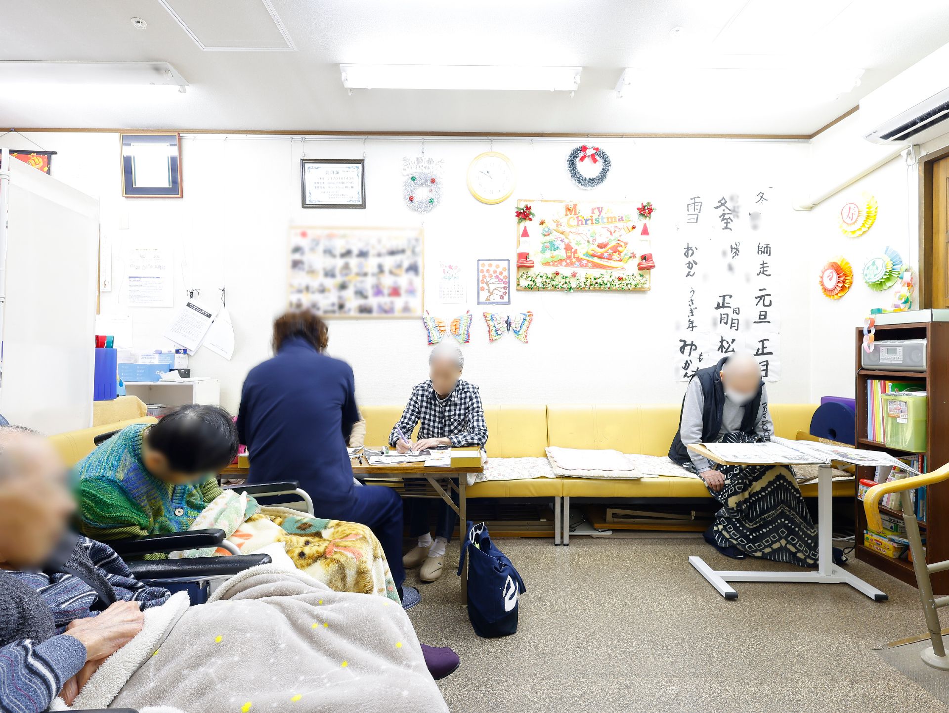 カルテにペンで書きこみながら話をしているエプロンを付けた若い女性スタッフ。そばには高齢女性がいる。