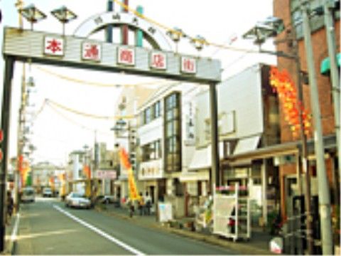 商店街のアーチがある。道路の真ん中には白線が引いてあり、端に車が停まっている。お店の前にはのぼりが立っている。