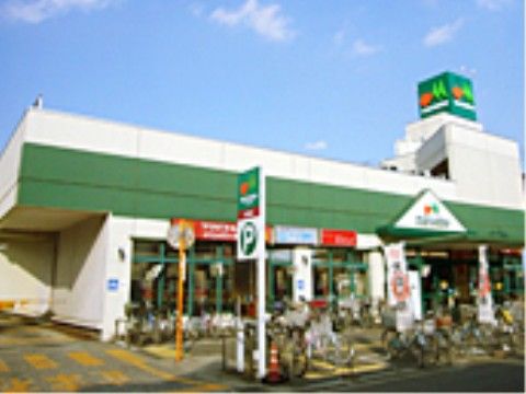 スーパーの前には自転車がたくさん停められていて、カーブミラーや駐車場の看板が立っている。建物の前面はガラス張りになっている。