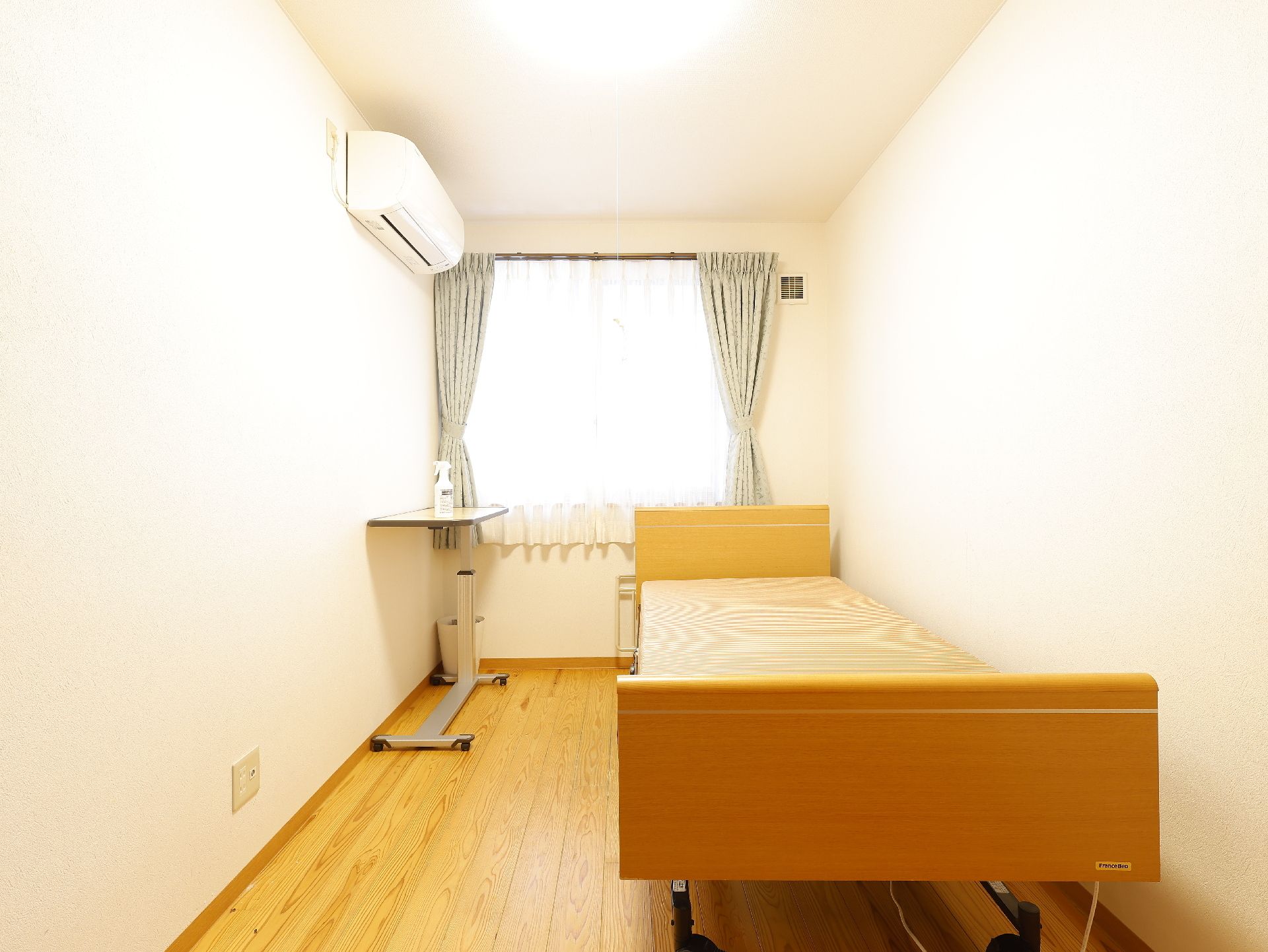 ピンクのエプロンを付けた若い女性スタッフに付き添われて、屋外での散歩を楽しんでいる車いすの高齢女性。