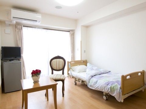 部屋の中央にはテーブルと椅子が置かれ、壁側にはキャスターのついたベッドがある。車椅子でもくつろげる広い居室内になっている。
