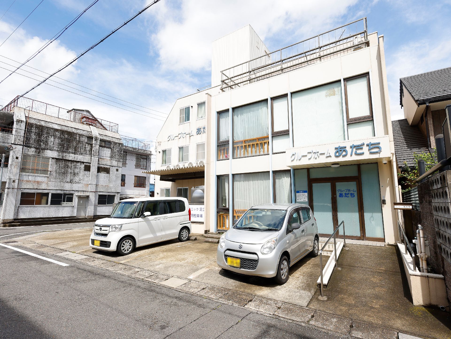 ピンクのエプロンを付けた若い女性スタッフが車いすの高齢女性に付き添い、散歩をしている。