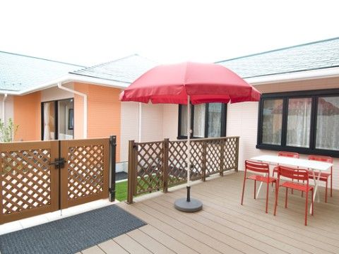 大きな赤色のパラソルが立っている、広さのあるウッドデッキ