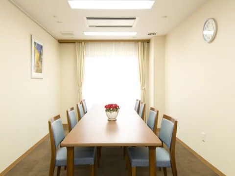 大きめのテーブルに、水色の座面と背もたれのついた椅子が６脚置かれている談話室
