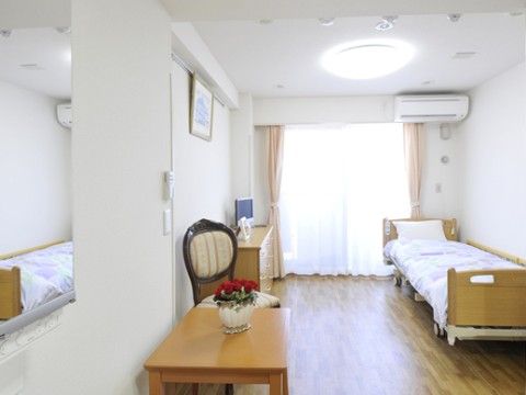 居室は、太陽光が差し込み日中は明るい。内装は白く、壁には絵画を飾っている。生活に必要な家具も備え付けている。