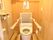温水洗浄便座が設置されたトイレが中央にあり、背もたれのパットが取り付けられた手すりが取り付けられている。